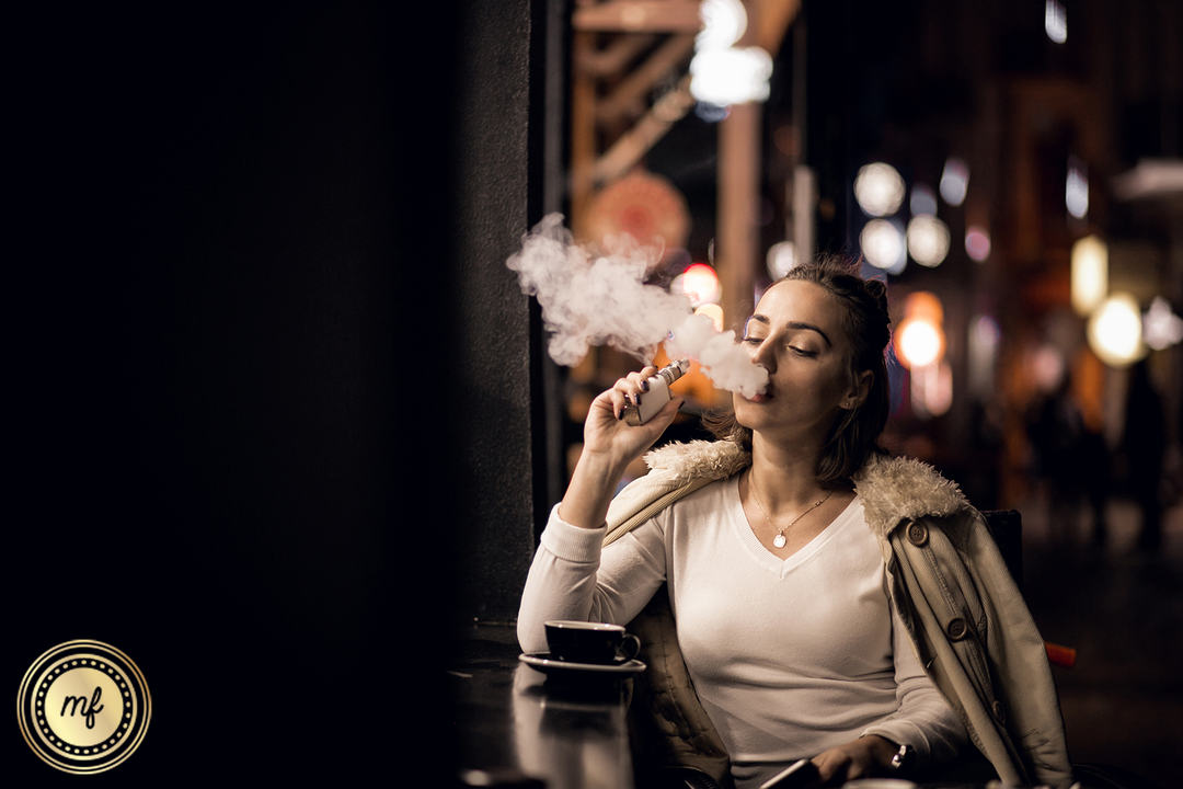 Woman sitting in a dark lounge taking a hit from a vape.