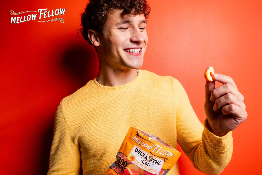A man holding a pack of Peach Ring flavored DELTA9 THC CBD gummies in his hand, picking a gummy to put in his mouth and smiling, against an orange background