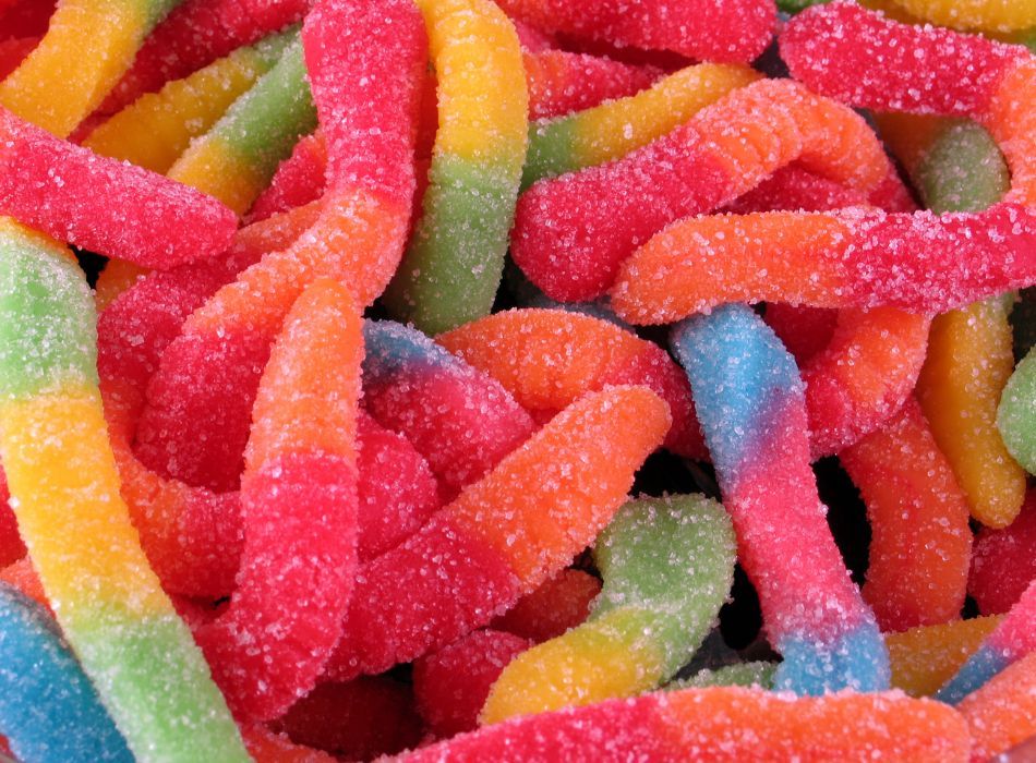 A pile of colorful gummy worms coated in sugar, featuring bright hues of red, orange, yellow, green, and blue