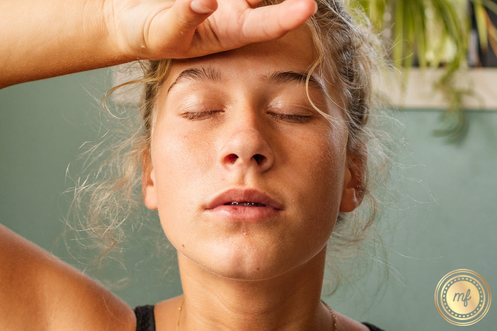Blonde woman with eyes closed touching her forehead with the back of her right hand.