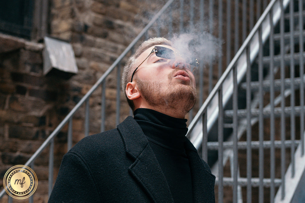 Man wearing sunglasses vaping outside next to a staircase.