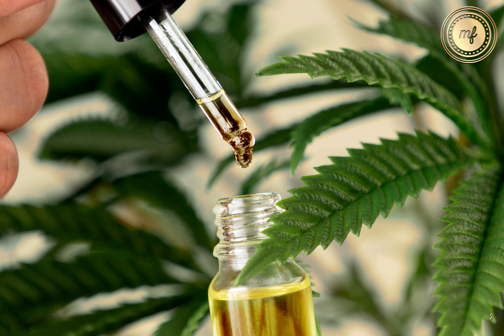Liquid drops from dropper into tincture, amidst cannabis leaves