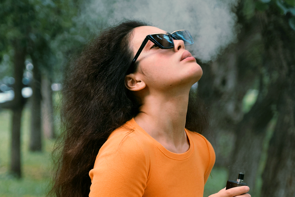 A lady holding a vape cartridge exhales smoke and enjoys the moment