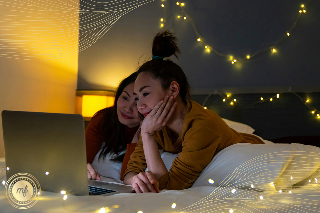 Two ladies are watching something on a laptop at night and smiling