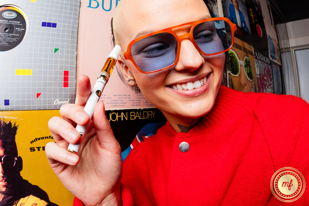 A lady smiling and holding a vape cartridge, wearing a red dress