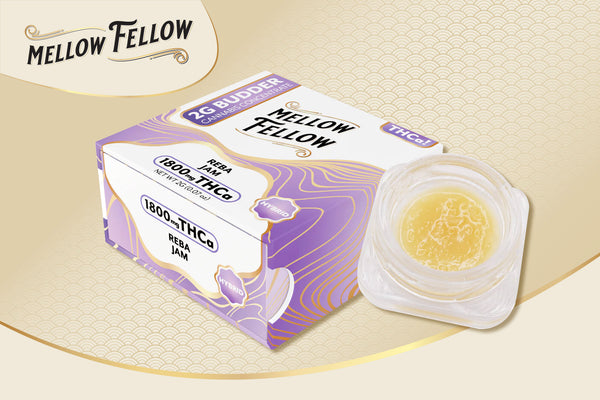 A small container of Mellow Fellow THC Budder is displayed alongside its packaging, which has a purple and gold design. The box indicates a 2g quantity. The background is a subtle gold pattern.