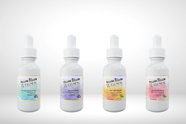 Four white dropper bottles labeled "Mellow Fellow Wellness" are displayed against a plain background. Each bottle has a different colored label: blue, purple, orange, and pink, indicating distinct blends or flavors.