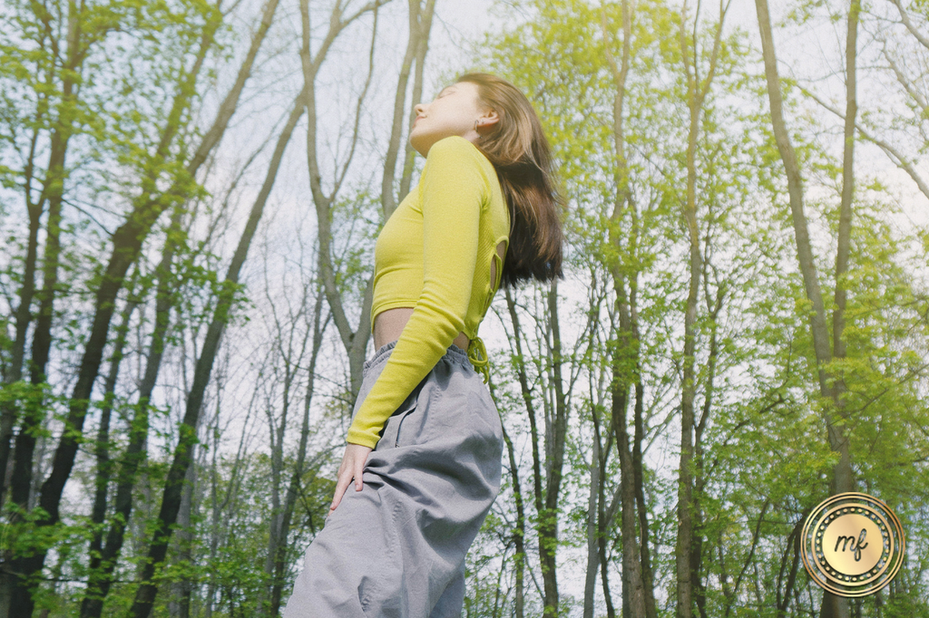 A lady wearing a lime-colored dress is standing in a place surrounded by lush green trees