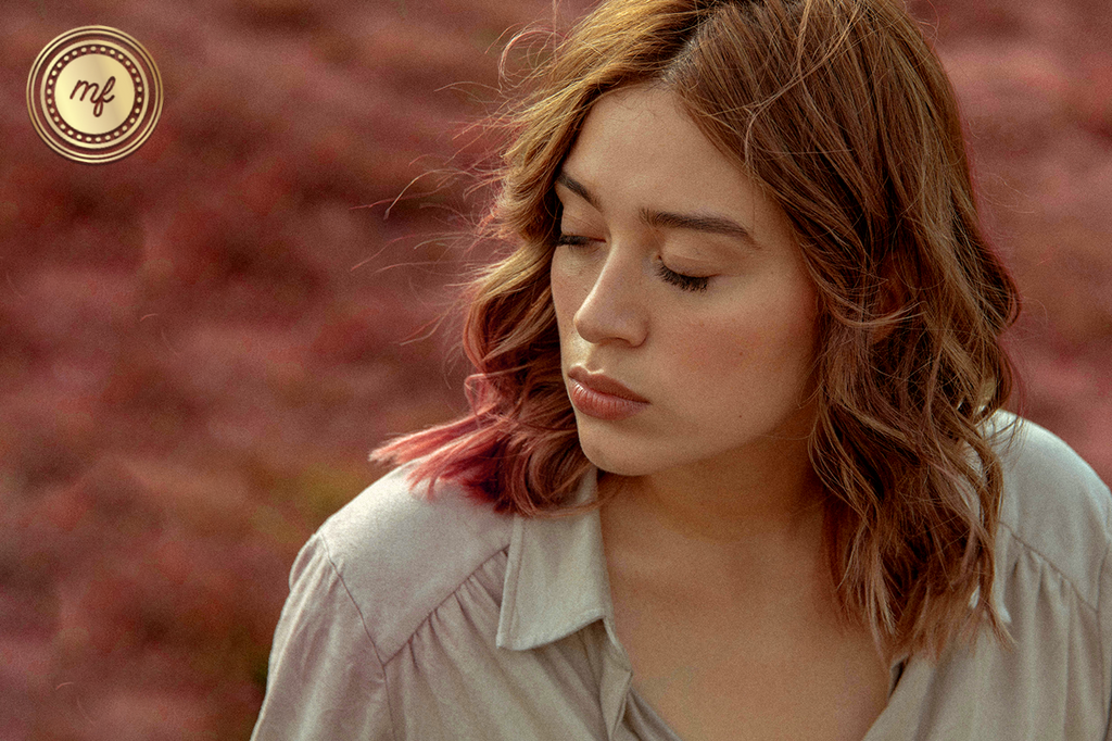 A woman is standing outdoors, closing her eyes and feeling the freshness