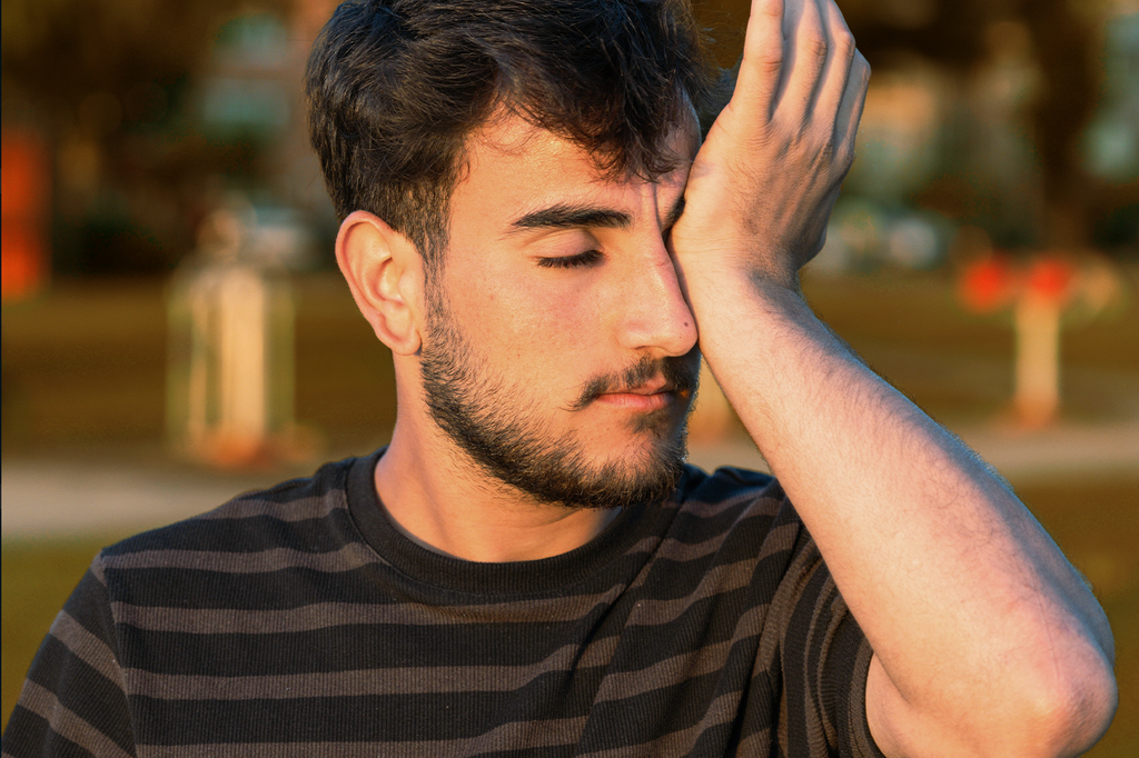 A man rubs his eyes with his hand as if they are itching