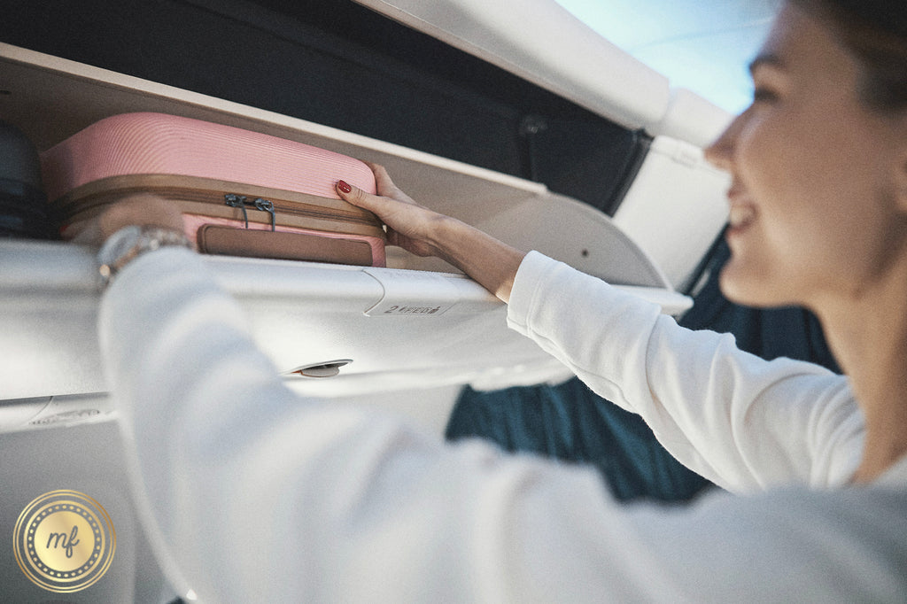 A lady puts her suitcase in the flight's overhead bin