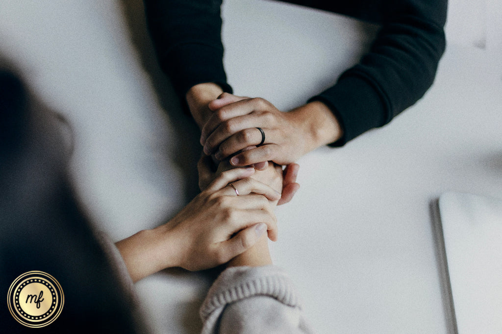 A girl and a boy sit across from each other, their hands gently intertwined on a white table