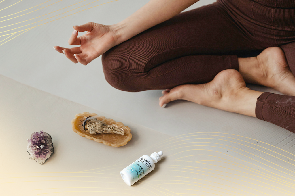 A person is meditating nearby an amethyst crystal, a sage bundle, and a Mellow Fellow Wellness:The Energy Blend