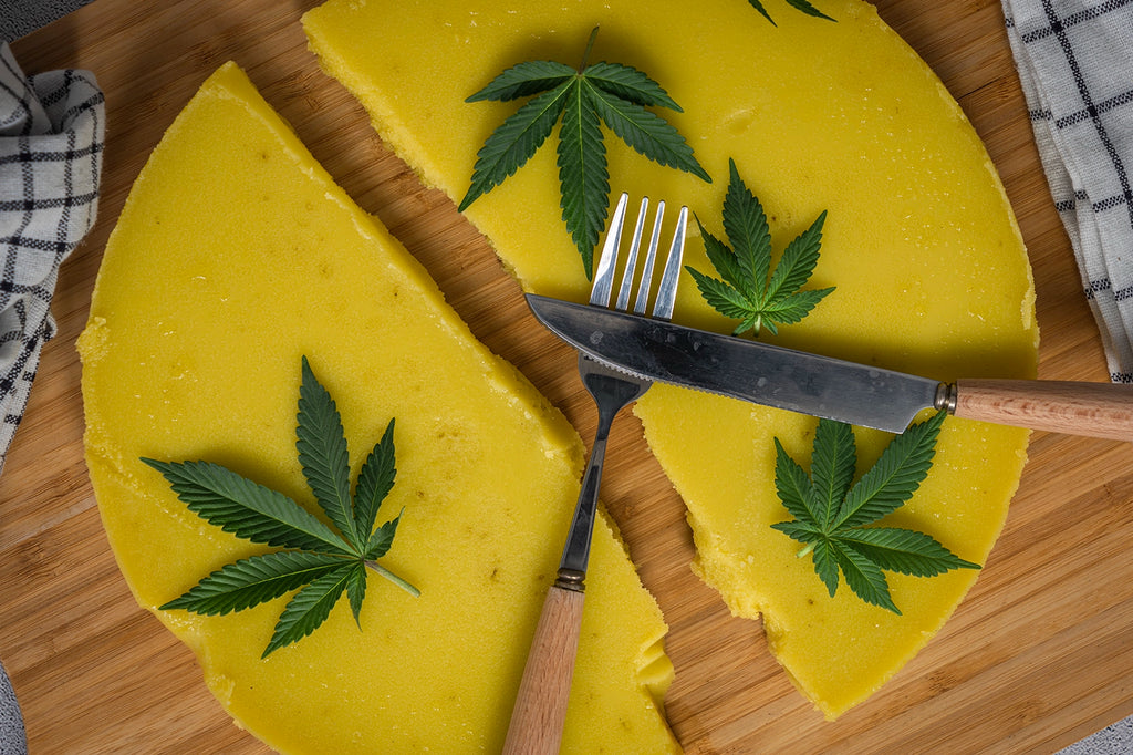 A yellow cannabis-infused cake with some cannabis leaves and two spoons placed on top