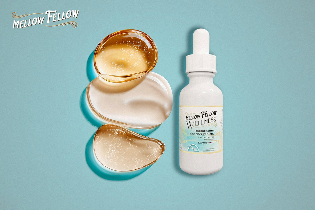 A Mellow Fellow WELLNESS Momentum energy blend bottle is set against a blue background, with three translucent, glossy liquid blobs beside it