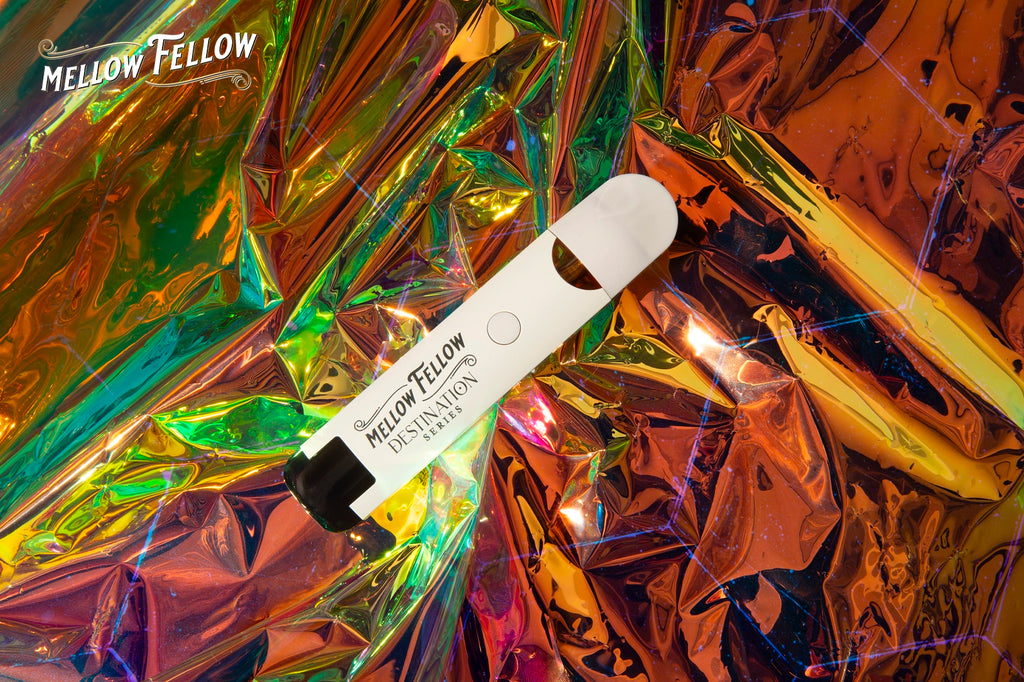 A Mellow Fellow DESTINATION series vape pen lies on vibrant, crumpled reflective holographic foil