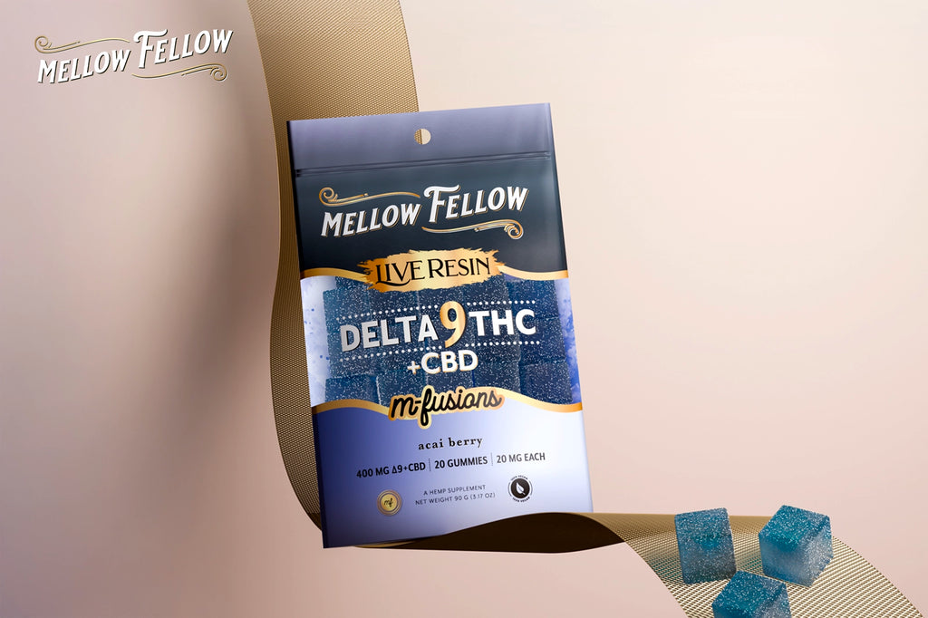 A pack of Mellow Fellow Live Resin Delta-9 THC M-Fusions in Acai Berry flavor sits on a gold ribbon, with blue gummies scattered around