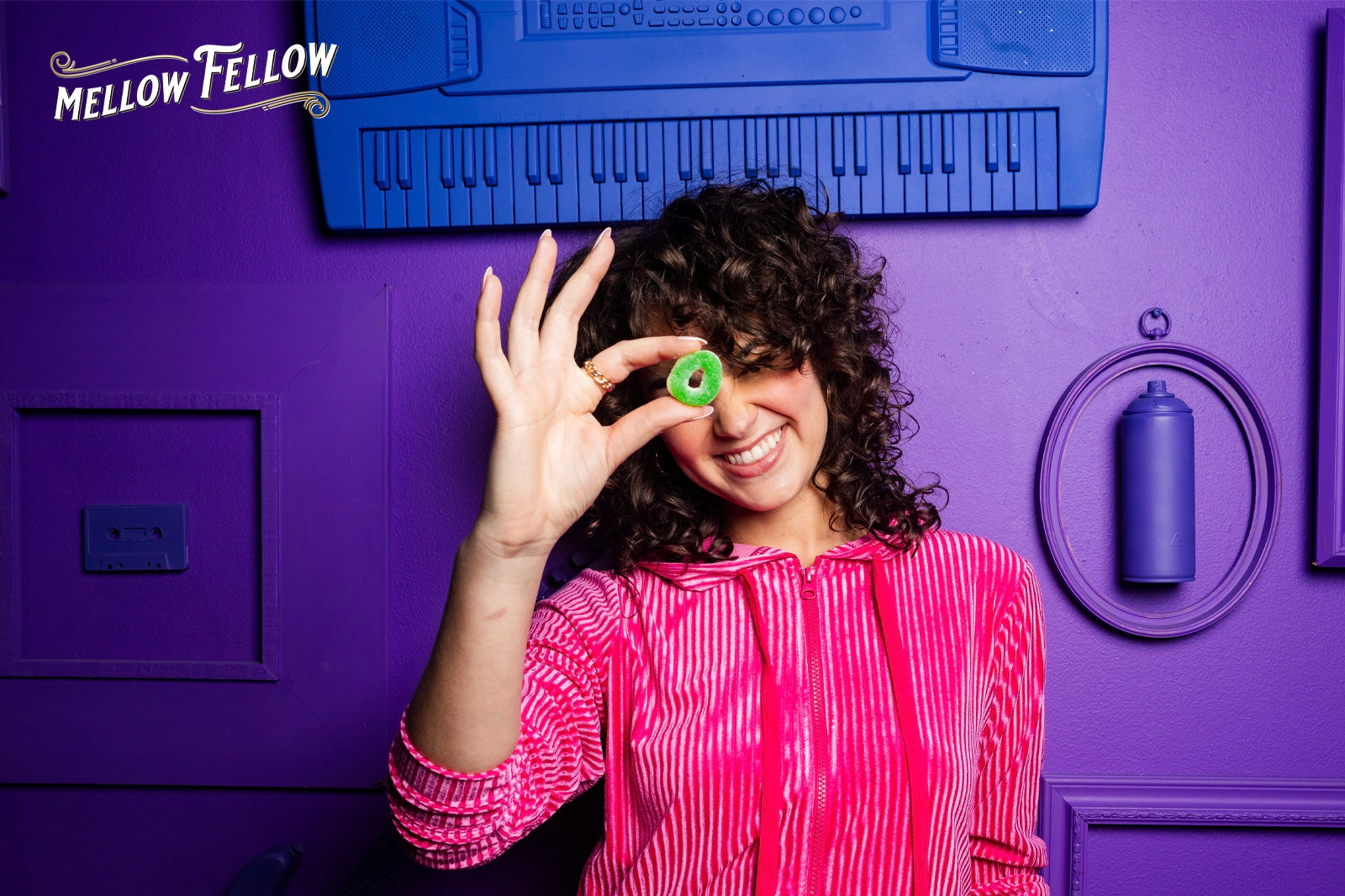 A lady holding green edible gummies in her hand, smiling, and standing against a purple background
