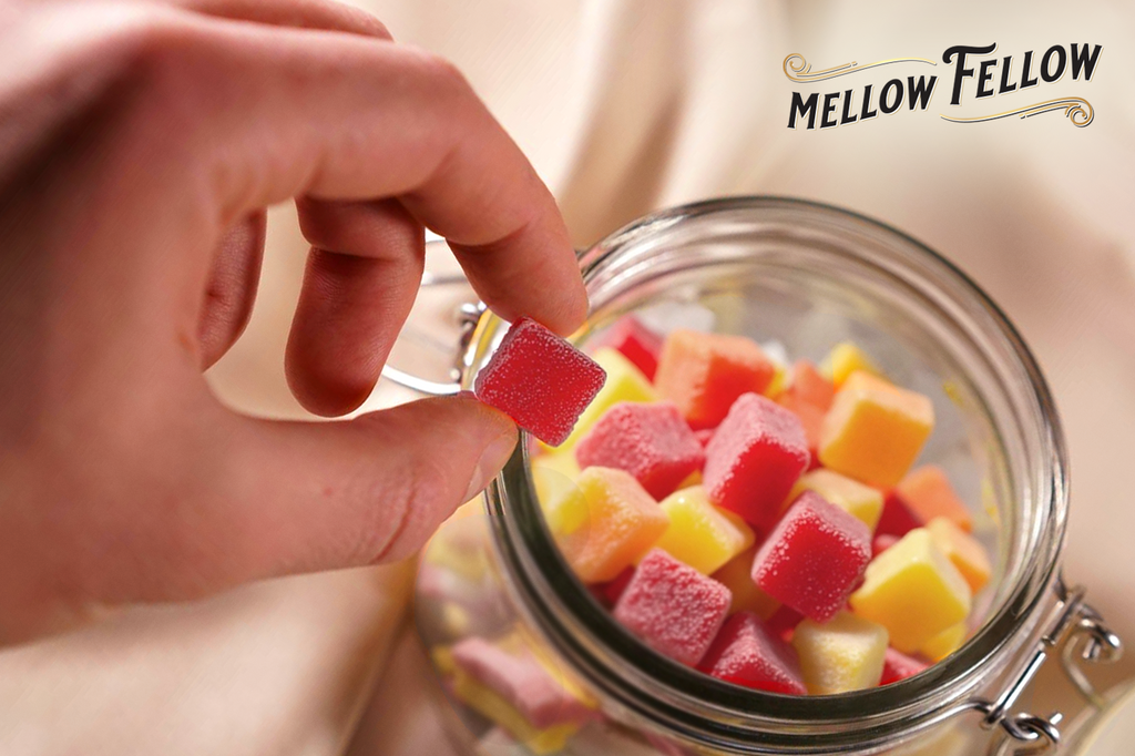 Yellow and red gummies in a glass container with someone picking one